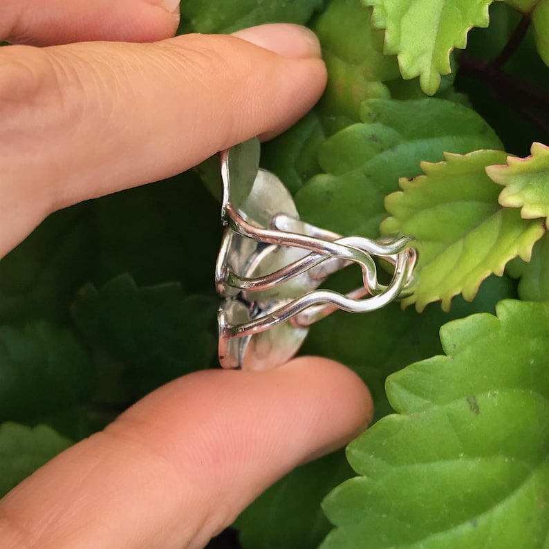 May include: A silver ring with a unique design featuring multiple intertwined bands and a round, slightly raised, silver centerpiece.