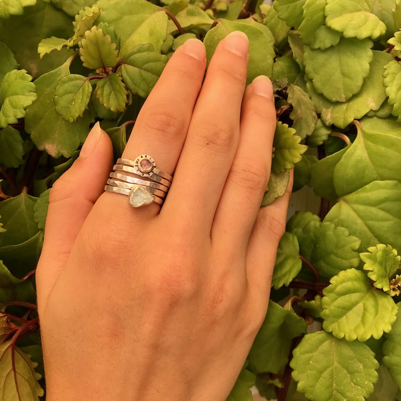 May include: A set of four silver rings with a pink gemstone and a clear stone. The rings are stacked on a finger.