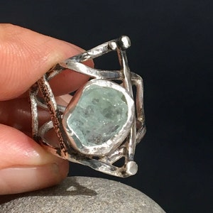 May include: A silver ring with a delicate, geometric design featuring a large, light blue aquamarine stone.