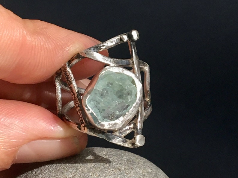 May include: A silver ring with a delicate, geometric design featuring a large, light blue aquamarine stone.