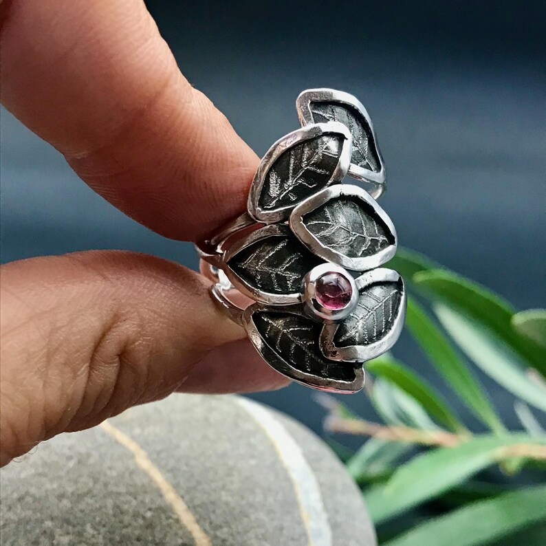 May include: A silver ring with a cluster of textured leaves and a pink gemstone in the center.