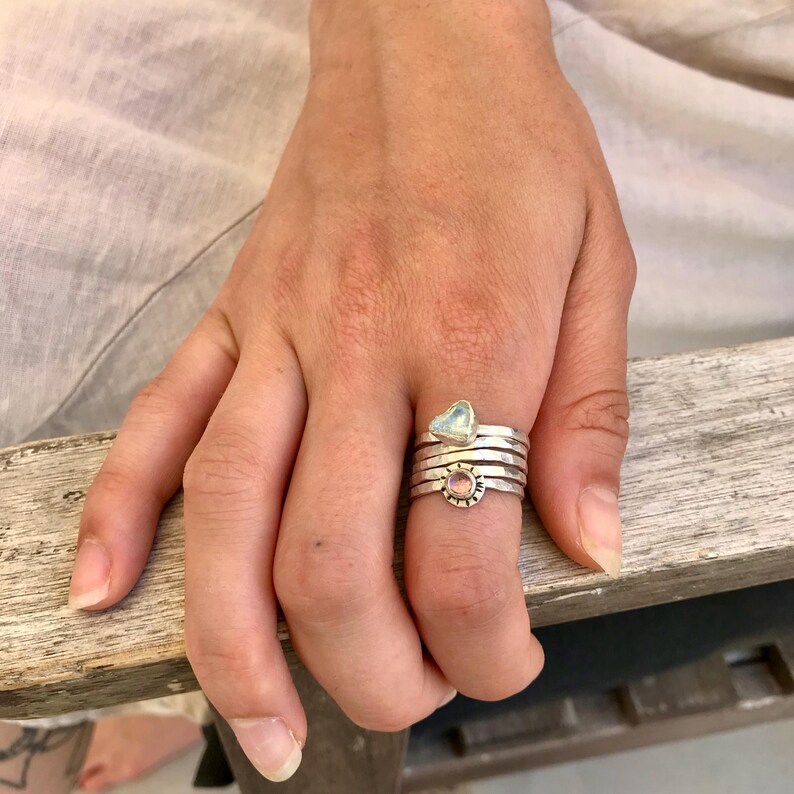 May include: A silver ring set with a stack of bands, featuring a small pink stone and a larger, triangular, iridescent stone.