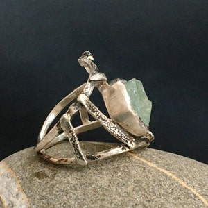 May include: A silver ring with a geometric design and a large, light green gemstone.