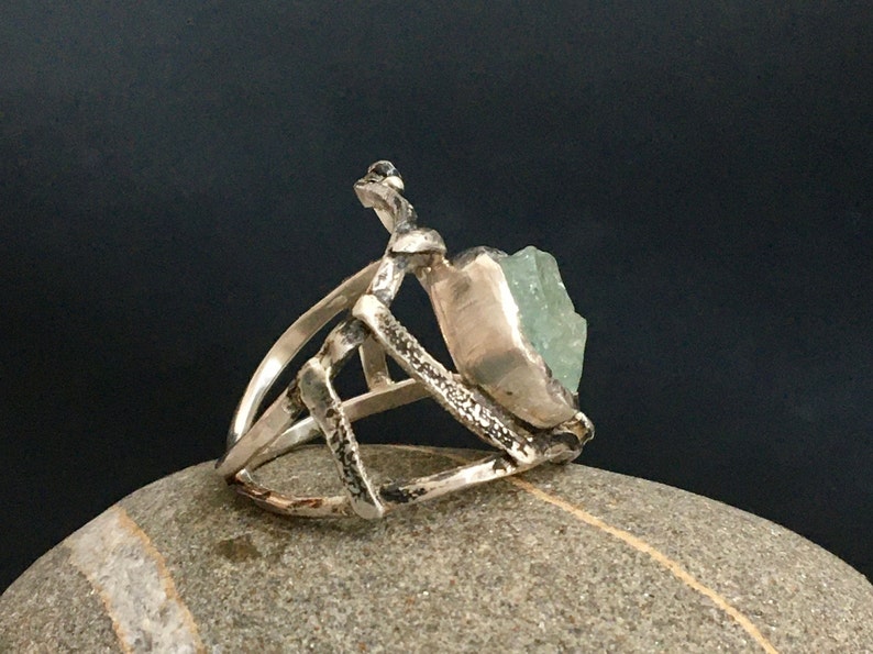 May include: A silver ring with a geometric design and a large, light green gemstone.