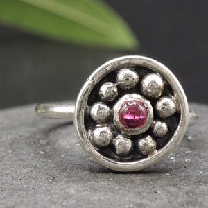 May include: A silver ring with a pink gemstone set in a circle of small silver beads.