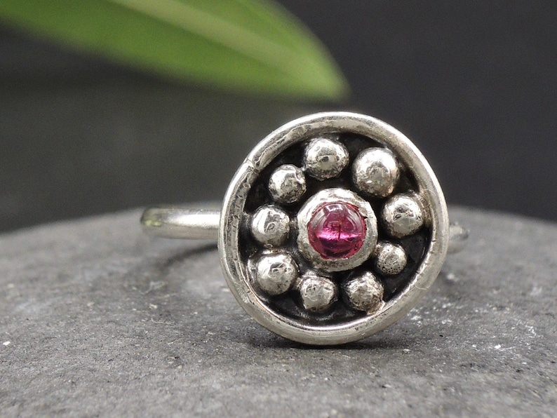 May include: A silver ring with a pink gemstone set in a circle of small silver beads.