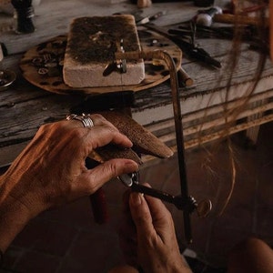 May include: A person uses a hand saw to cut a piece of metal. The metal is clamped in a vise. The person is wearing several rings on their fingers.