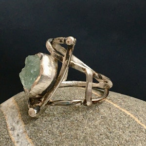 May include: A silver ring with a large, green, faceted gemstone set in a textured silver bezel. The ring band is made of twisted silver wire.