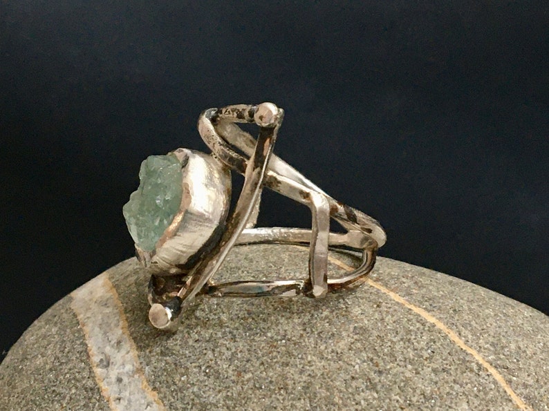 May include: A silver ring with a large, green, faceted gemstone set in a textured silver bezel. The ring band is made of twisted silver wire.
