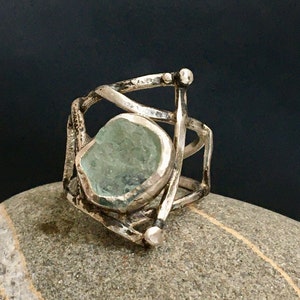 May include: A silver ring with a large, light blue aquamarine stone set in a cage-like design.