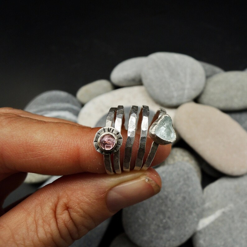 May include: A set of four silver rings with hammered textures. One ring features a pink gemstone, while another has a light blue gemstone.