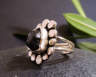 May include: A silver ring with a black gemstone set in a flower-shaped design. The ring has a double band and is made of sterling silver.