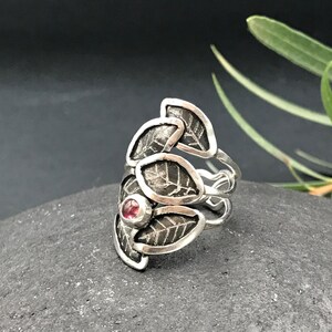 May include: A silver ring with a textured leaf design and a pink gemstone in the center.