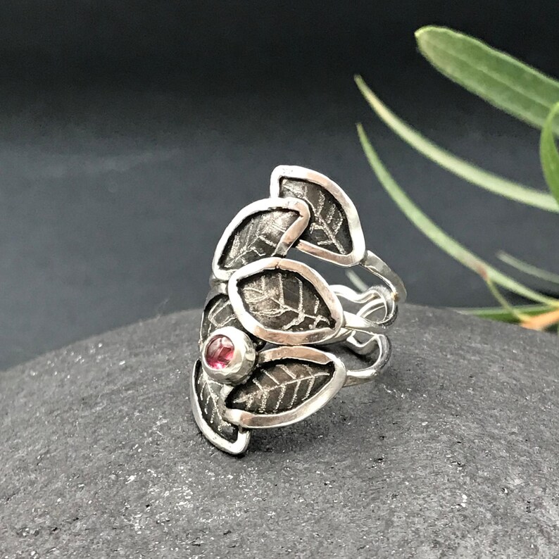 May include: A silver ring with a textured leaf design and a pink gemstone in the center.