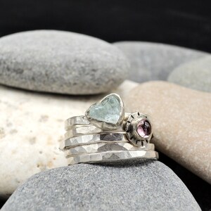 May include: A set of five silver stacking rings with a light blue heart-shaped gemstone and a pink gemstone set in a silver bezel.