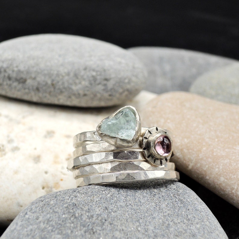 May include: A set of five silver stacking rings with a light blue heart-shaped gemstone and a pink gemstone set in a silver bezel.