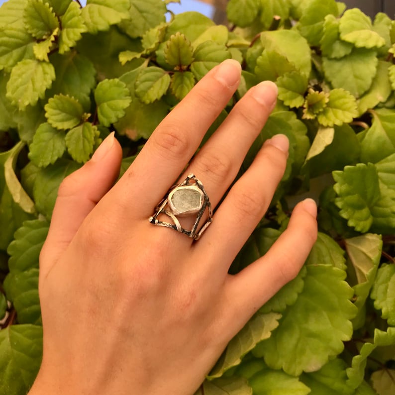 May include: A silver ring with a large, irregular, light green gemstone set in a geometric design.