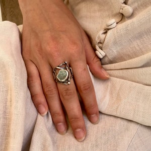 May include: A silver ring with a geometric design featuring a large, irregular, light green stone.