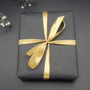 May include: A black gift box with a gold ribbon tied in a bow.