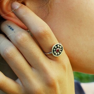 May include: A silver ring with a red gemstone in the center surrounded by small silver beads.