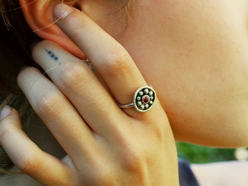 May include: A silver ring with a red gemstone in the center surrounded by small silver beads.