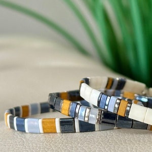 May include: Three stacked bracelets with a pattern of white, blue, and yellow beads.
