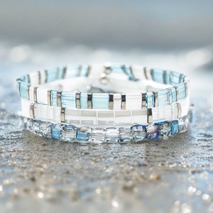 May include: A stack of three bracelets made with blue and white glass beads. The bracelets are layered on top of each other and have a silver clasp.