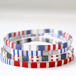 May include: Three stacked bracelets with red, white, and blue patterned tiles. The bracelets are made of metal and have a silver finish.