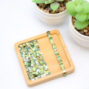 May include: A wooden tray with a pile of green and gold square glass beads and a single strand of green and gold square glass beads.