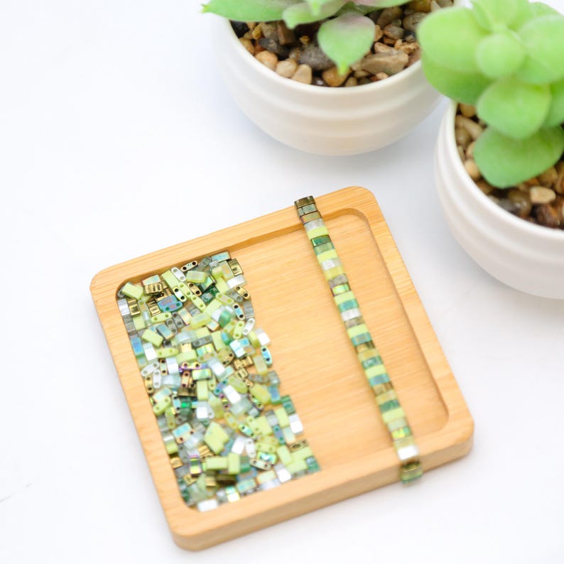 May include: A wooden tray with a pile of green and gold square glass beads and a single strand of green and gold square glass beads.