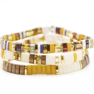May include: A set of three bracelets with yellow, white, brown, and iridescent beads. The bracelets are stacked on top of each other.