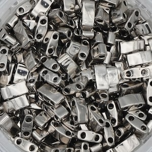 May include: A close-up of a pile of silver metal beads. The beads are rectangular with two holes on each side. The beads are shiny and have a metallic finish.