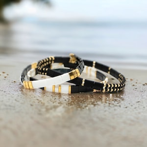 May include: Three stacked bracelets with black and white tiles and gold accents. The bracelets are made of a durable material and are perfect for everyday wear.