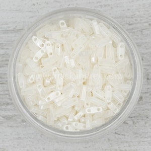 May include: A clear glass jar filled with white opaque glass beads. The beads are small and rectangular with two holes in each bead.