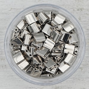 May include: A clear plastic container filled with silver metal beads. The beads are square shaped with four holes in each bead.