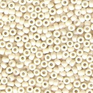 May include: Close-up of a pile of small, off-white seed beads. The beads are cylindrical with a hole running through the center, and are scattered randomly. The beads are uniform in size and shape, creating a textured surface.