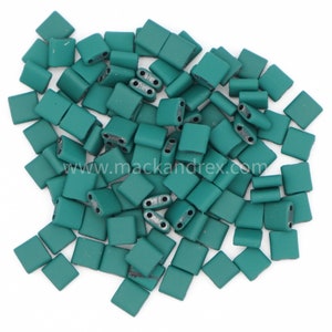 May include: A pile of teal green square beads with two holes in each bead.