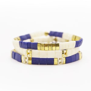 May include: Three stacked bracelets with white and blue ceramic beads and gold accents.