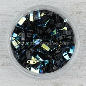 May include: A close-up view of a glass jar filled with black and iridescent glass beads. The beads are rectangular in shape and have a variety of colors, including blue, green, and gold.