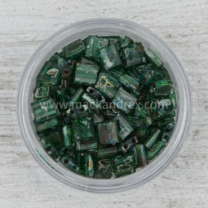 May include: A close-up of a clear container filled with green and gold square glass beads. The beads have a speckled and iridescent finish.