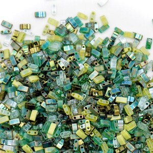 May include: A large assortment of green, yellow, and clear glass seed beads. The beads are all rectangular in shape and have two holes.