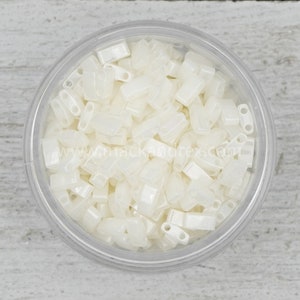 May include: A clear plastic container filled with opaque white rectangular beads with two holes on one end. The beads are approximately 1/4 inch long.