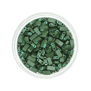 May include: A close-up view of a glass jar filled with small, dark green rectangular beads with a light blue edge. The beads have two holes in each.