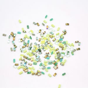 May include: Assortment of small, rectangular glass beads in shades of green, yellow, and clear. The beads have a slightly iridescent finish.