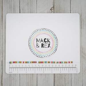 May include: A colorful beaded bracelet with turquoise, pink, and gold accents is displayed on a white card with a ruler. The card also features a circular logo with the text "MACK & REX" in a playful font. The bracelet measures approximately 7 inches in length.