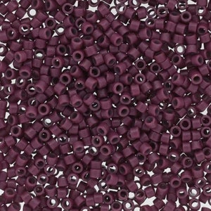 May include: Close-up of a pile of small, cylindrical beads in a deep plum color. Each bead has a hole running through the center, and they are scattered randomly, creating a textured surface. These beads are suitable for jewelry making and crafts.