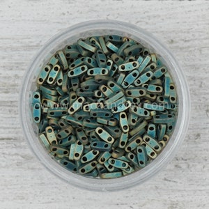 May include: A close-up view of a container filled with teal and gold-toned metal beads. The beads are small and have a rectangular shape with two holes in each bead.