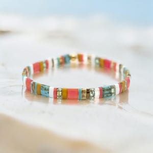 May include: A colorful beaded bracelet with a mix of turquoise, pink, yellow, white, and gold beads.