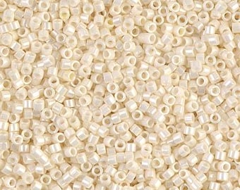 May include: A close-up shot of a pile of small, off-white, cylindrical beads. The beads have a slightly iridescent sheen, reflecting light. These beads are likely used for jewelry making or other craft projects.