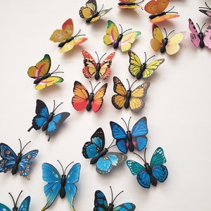 May include: A collection of colorful butterfly decorations in various sizes and designs. The butterflies feature shades of yellow, orange, red, pink, and blue. Each butterfly has a black body and antenna, creating a vibrant and eye-catching display.